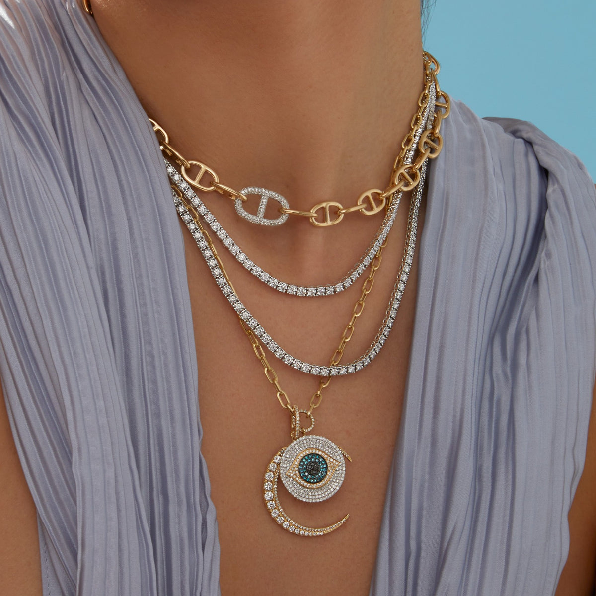 Model wearing diamond tennis necklaces, anchor chain link necklace, gold chain link necklace with diamond evil eye and moon charm