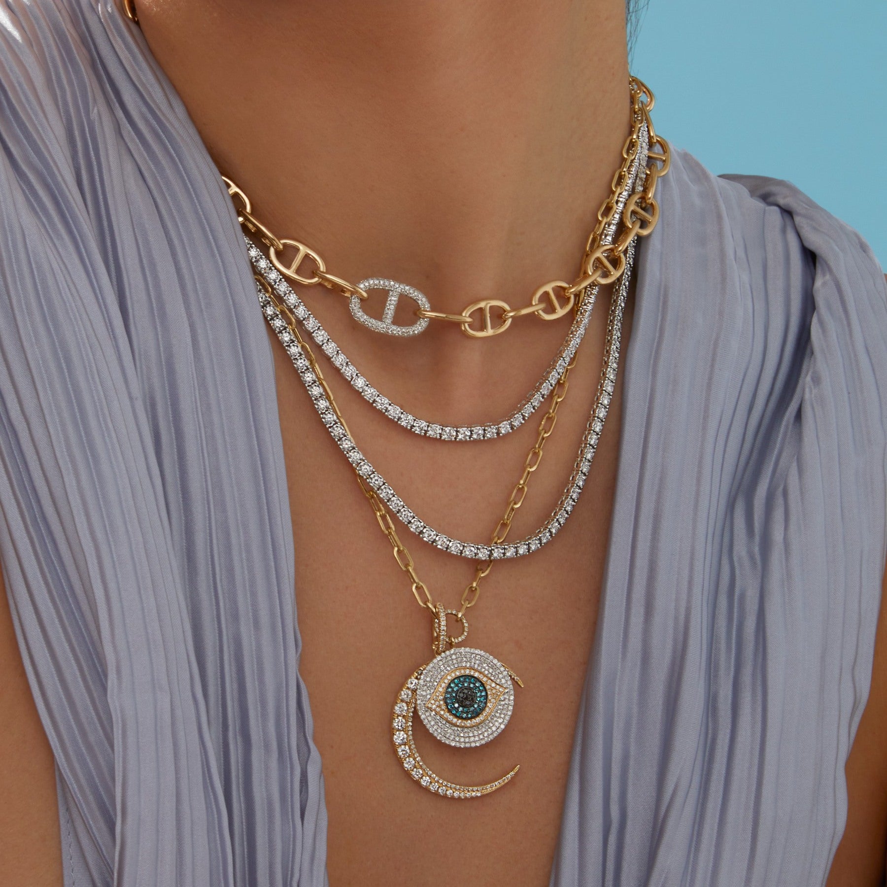 Model wearing diamond tennis necklaces, anchor chain link necklace, gold chain link necklace with diamond evil eye and moon charm