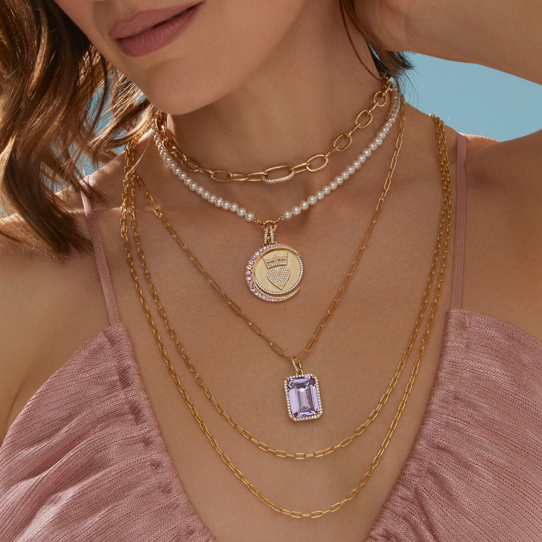 Model wearing chain link necklaces in multiple lengths layered with diamond gold pink sapphire charms