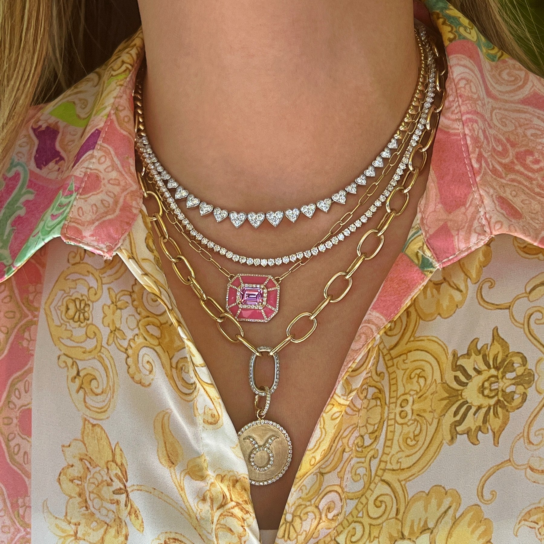 Heart diamond necklace, diamond tennis necklace, pink topaz enamel necklace, yellow gold chain link and diamond necklace with taurus zodiac charm layered on model