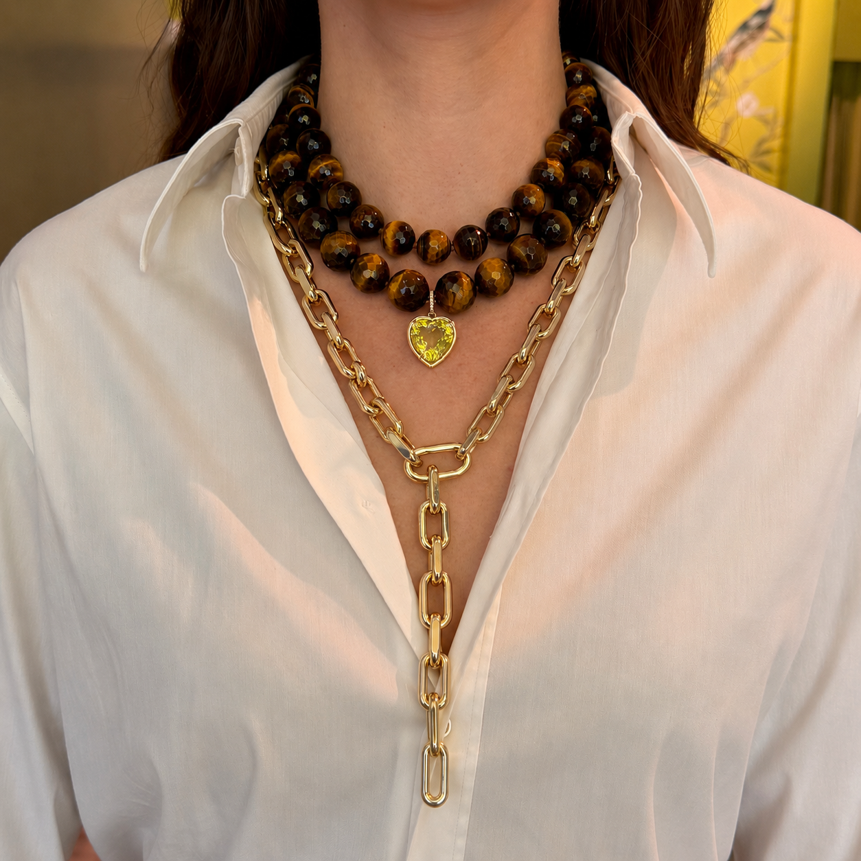 Person wearing tiger beaded necklaces layered with lemon topaz heart charm and luxe roma necklaces