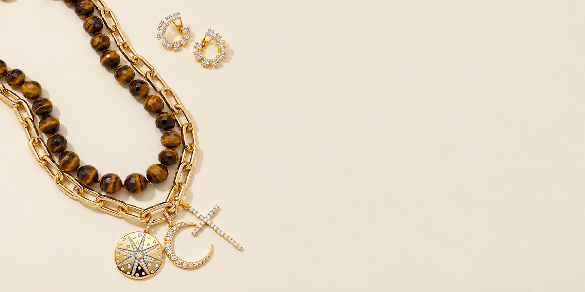 Tiger's Eye Beaded Necklace & 14KT Luxe Roma Gold Chain Link Necklace with Star, Moon and Cross Charms and Marceline Baguette Diamond Earrings set on a cream background